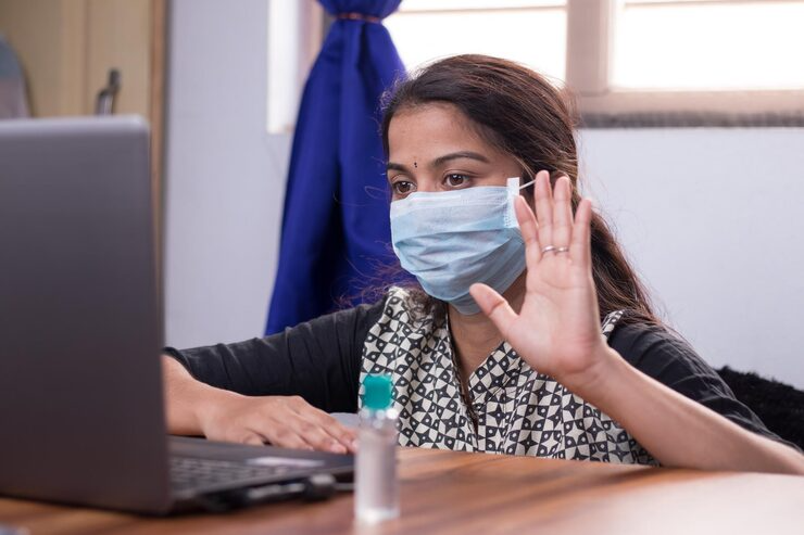 Woman in mask waving at laptop-Bridge Health (contact)